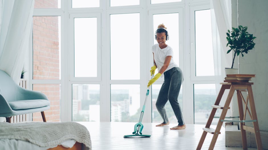 Woman cleaning a bright room with a mop, enjoying music with headphones.